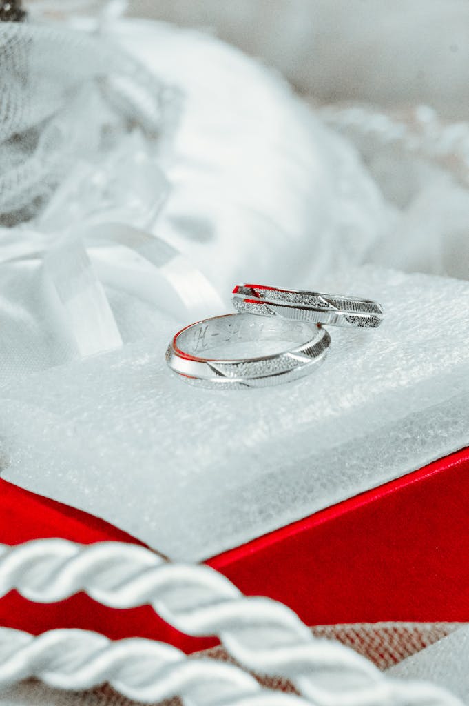 Close-up of elegant silver wedding rings on a white cushion with a red box, symbolizing love and commitment.